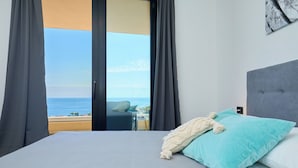 A bedroom with a large bed, a view of the sea, and a balcony.