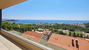 A balcony with a clear view of a coastal town, terracotta-roofed buildings, and a distant sea.