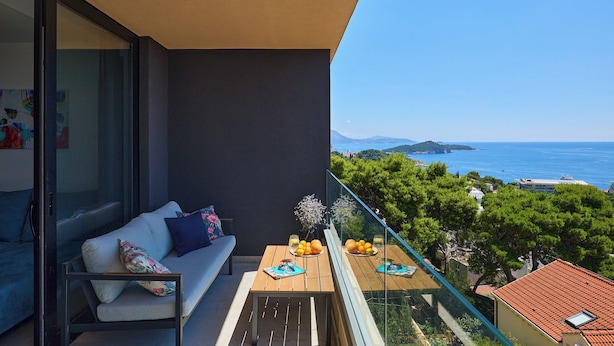 A balcony with a sofa, a table with fruits and glasses, and a view of the sea and greenery.