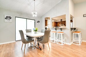 Una cocina moderna con armarios de madera, un refrigerador de acero inoxidable y un comedor con una mesa blanca y sillas grises.
