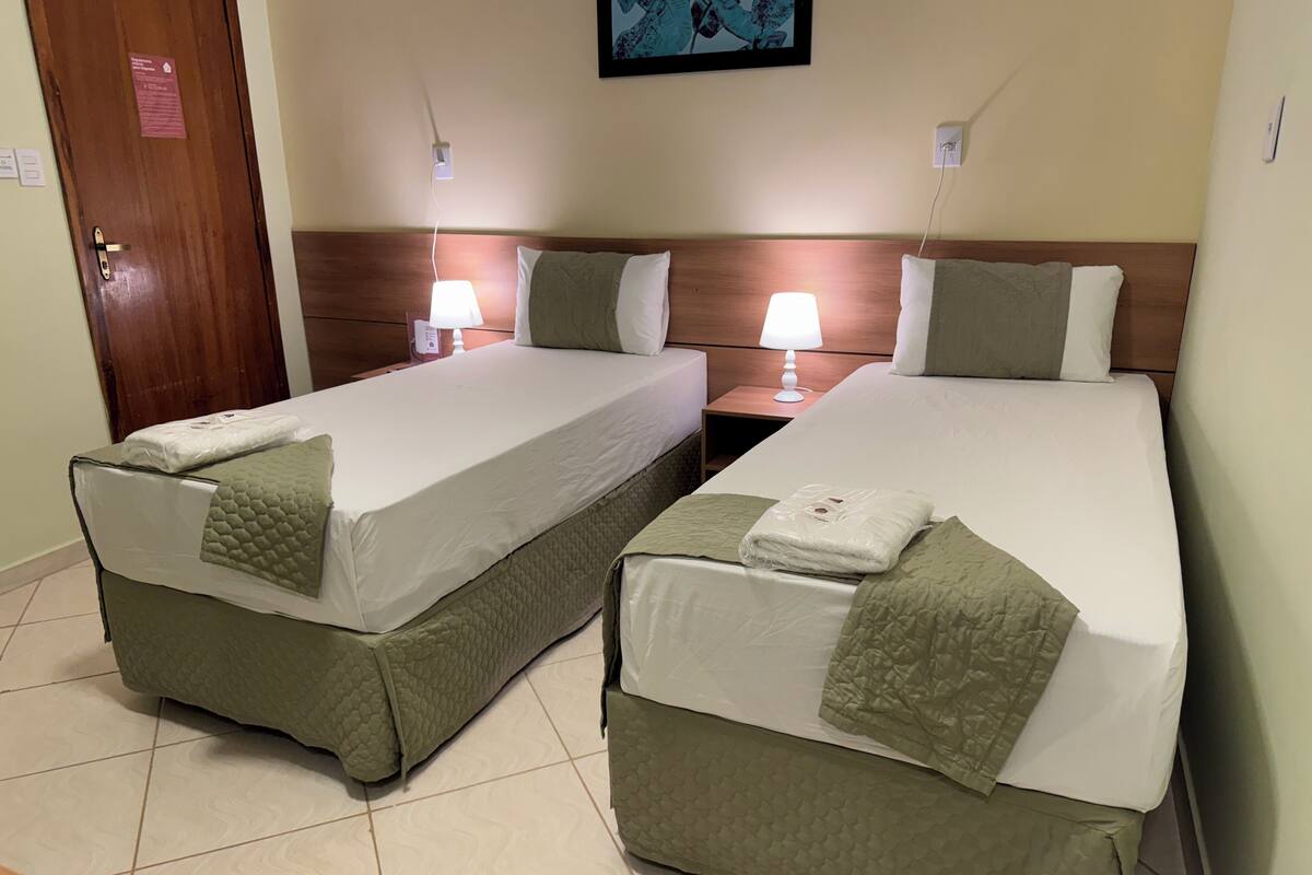 Two single beds with headboards, bedside tables with lamps, and a door with a sign.