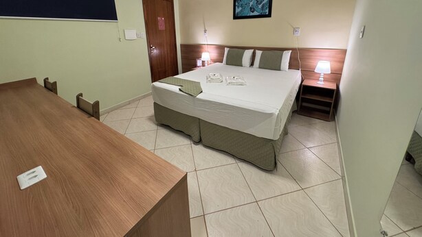 A hotel room with a bed, bedside table, and a wooden desk. -  Domus Hotel Palmeiras - Canaã dos Carajás (Canaa dos Carajas)