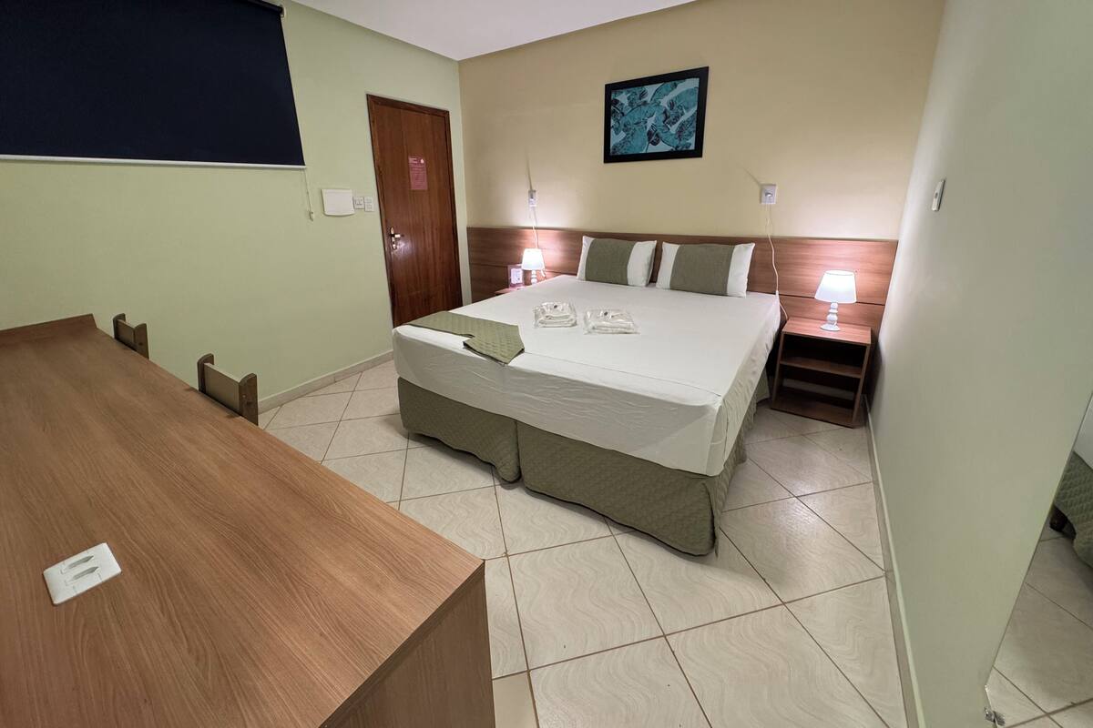 A hotel room with a bed, bedside table, and a wooden desk.