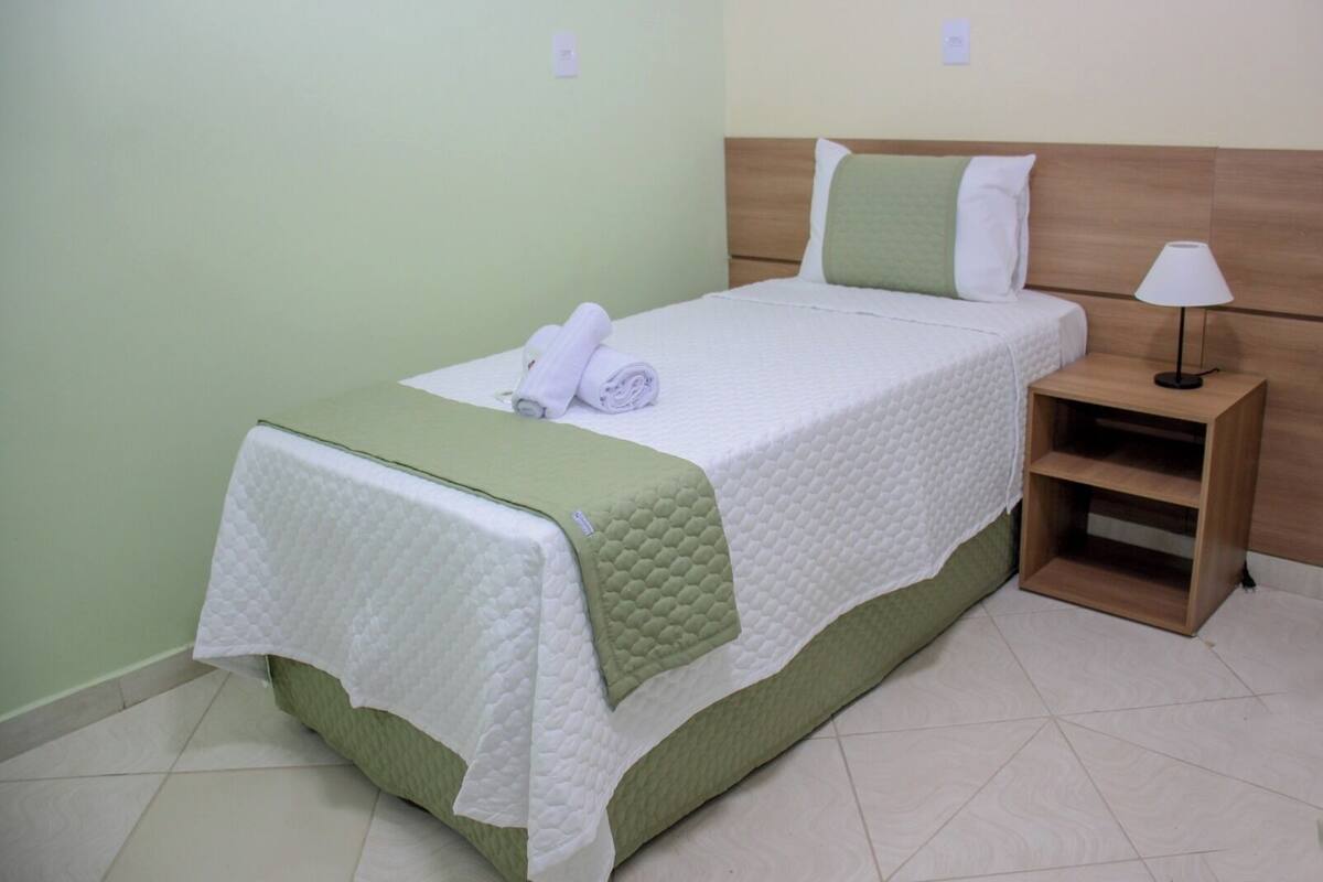 A neatly made bed with a green and white quilt, a wooden nightstand with a lamp, and a green pillow.
