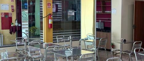 Un restaurant amb taules i cadires metàl·liques, un extintor i una partició de vidre.