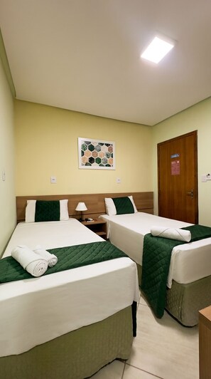 Habitación de hotel con dos camas, una mesita de noche, una lámpara, un cuadro en la pared y una puerta con un cartel.