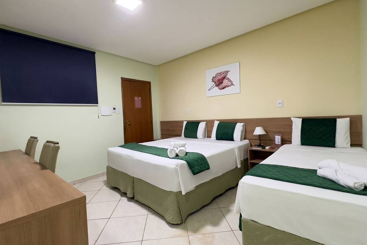 A hotel room with two beds, a desk, and a window with a blue blind.