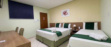 A hotel room with two beds, a desk, and a window with a blue blind.