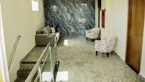 A lobby with a marble wall, a sofa, two patterned chairs, a wooden door, and a staircase with metal railings. -  Domus Hotel Palmeiras - Canaã dos Carajás (Canaa dos Carajas)