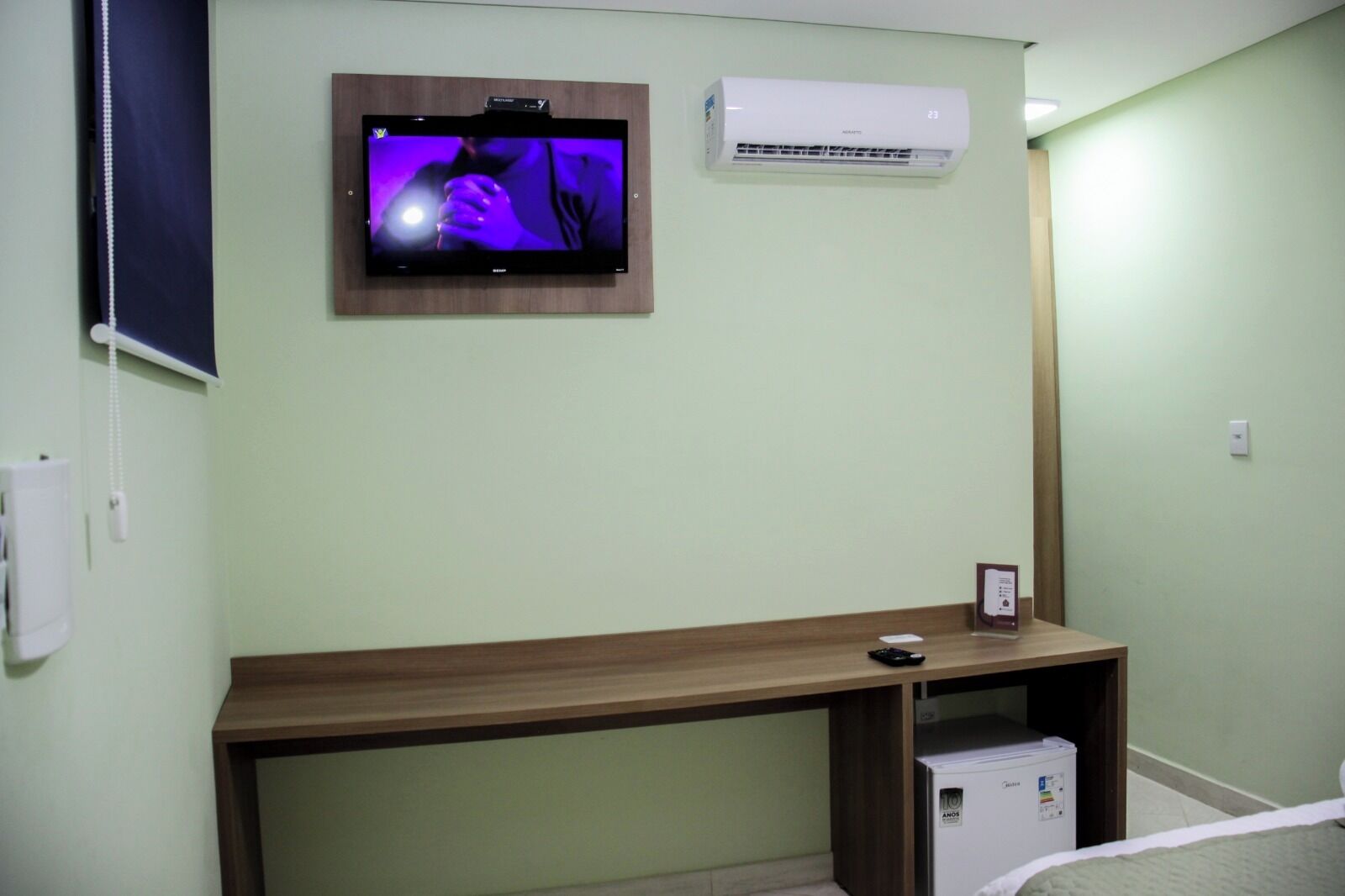 Ein Zimmer mit einem Holztisch, einem Wand-Fernseher, einer Klimaanlage und einem kleinen Kühlschrank.