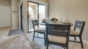 A dining area with a table set for two, chairs, a rug, and a view through a glass door to an outdoor patio.