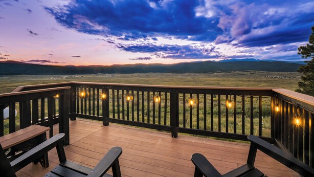 Una terraza de madera con bancos que da a un paisaje cubierto de hierba y montañas lejanas bajo un cielo nublado.