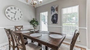 A dining room with a wooden table, four chairs, a clock, a chandelier, and artwork on the walls. - Country Oasis w/ Game Rm, Mins from DWTN & Airport (North Charleston)