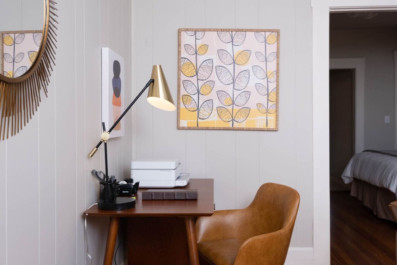 A room with a desk, a chair, a lamp, and artwork on the wall.
