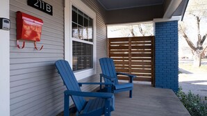 Un porche con dos sillas Adirondack azules, un buzón rojo y un portón de madera.