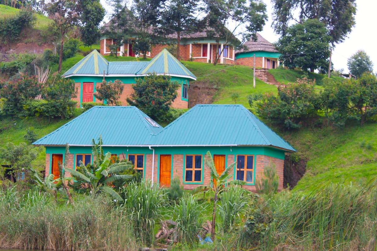 A house with a green roof and orange doors, surrounded by lush greenery and a body of water.