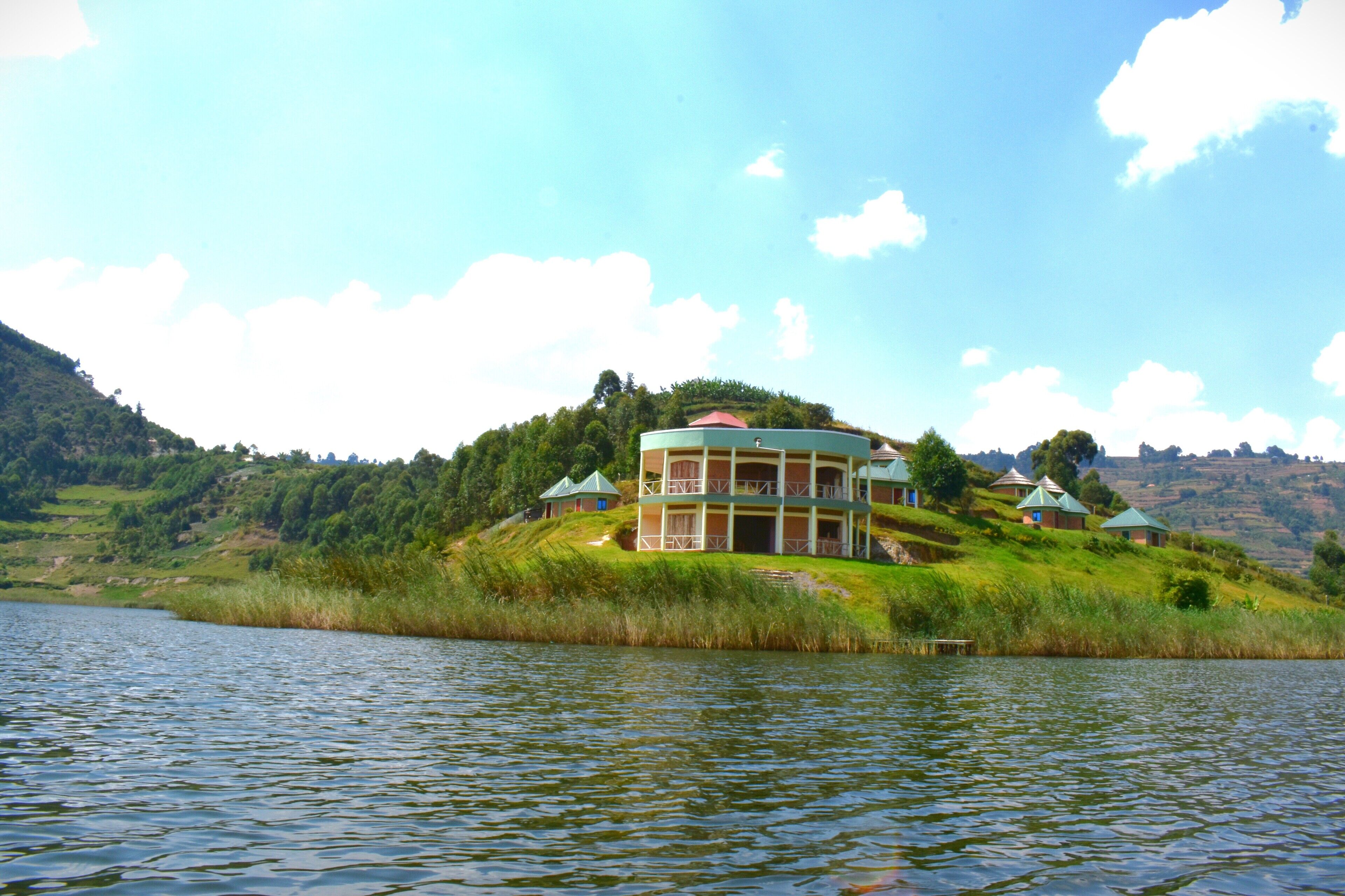 A lakeside property with a central building surrounded by smaller structures, set against a backdrop of hills and a clear sky.