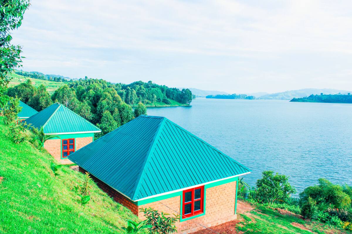 A lakeside property with two cottages, each featuring a green roof and red-framed windows.