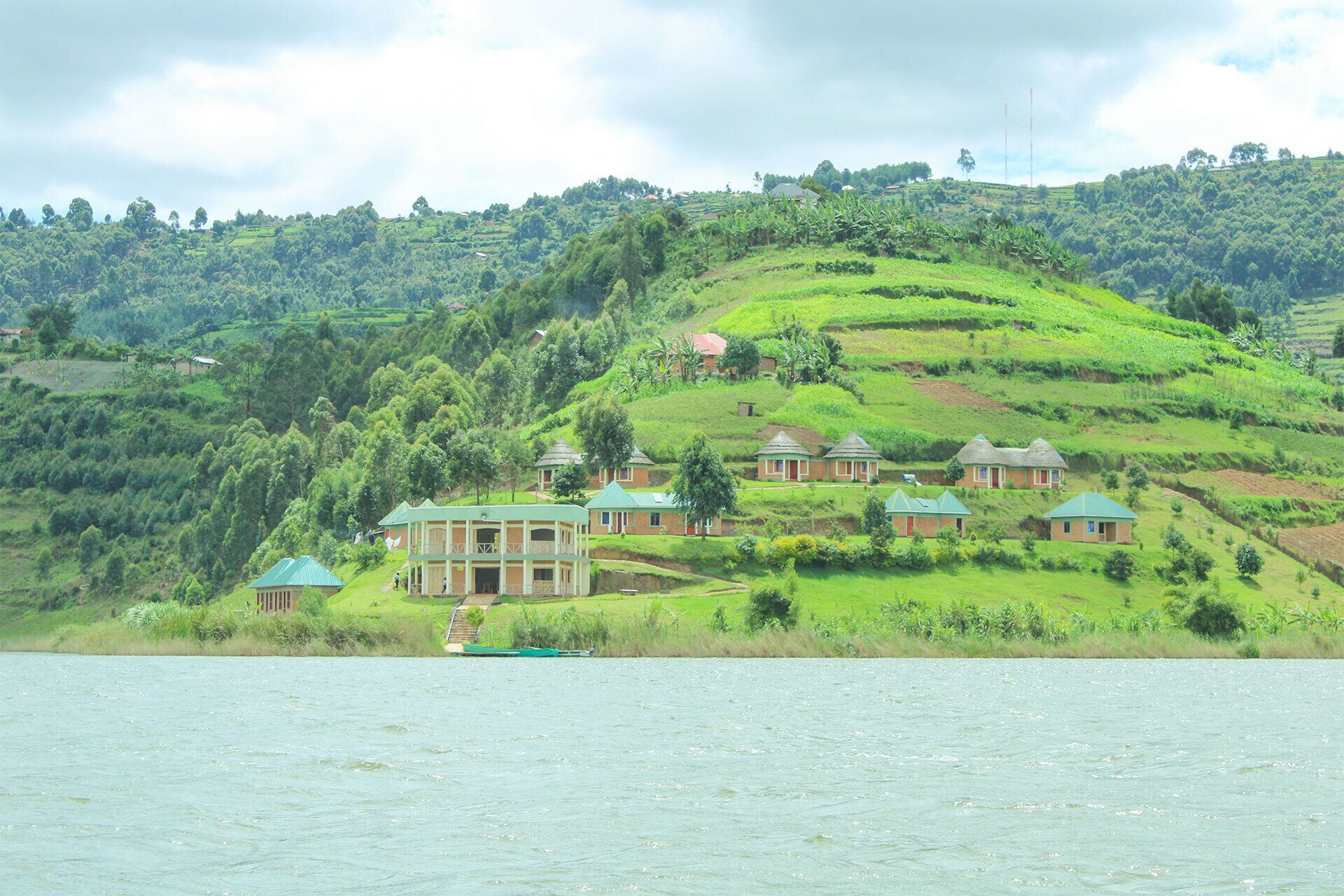 A hillside with several buildings, likely a resort, featuring multiple structures with green roofs, situated near a body of water.