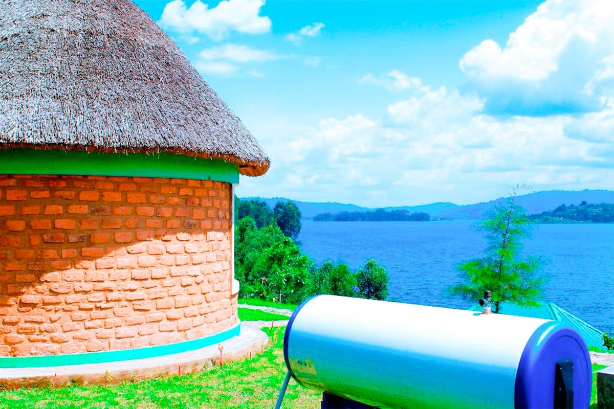 A brick building with a thatched roof, a cylindrical object in front, and a lake with hills in the background.