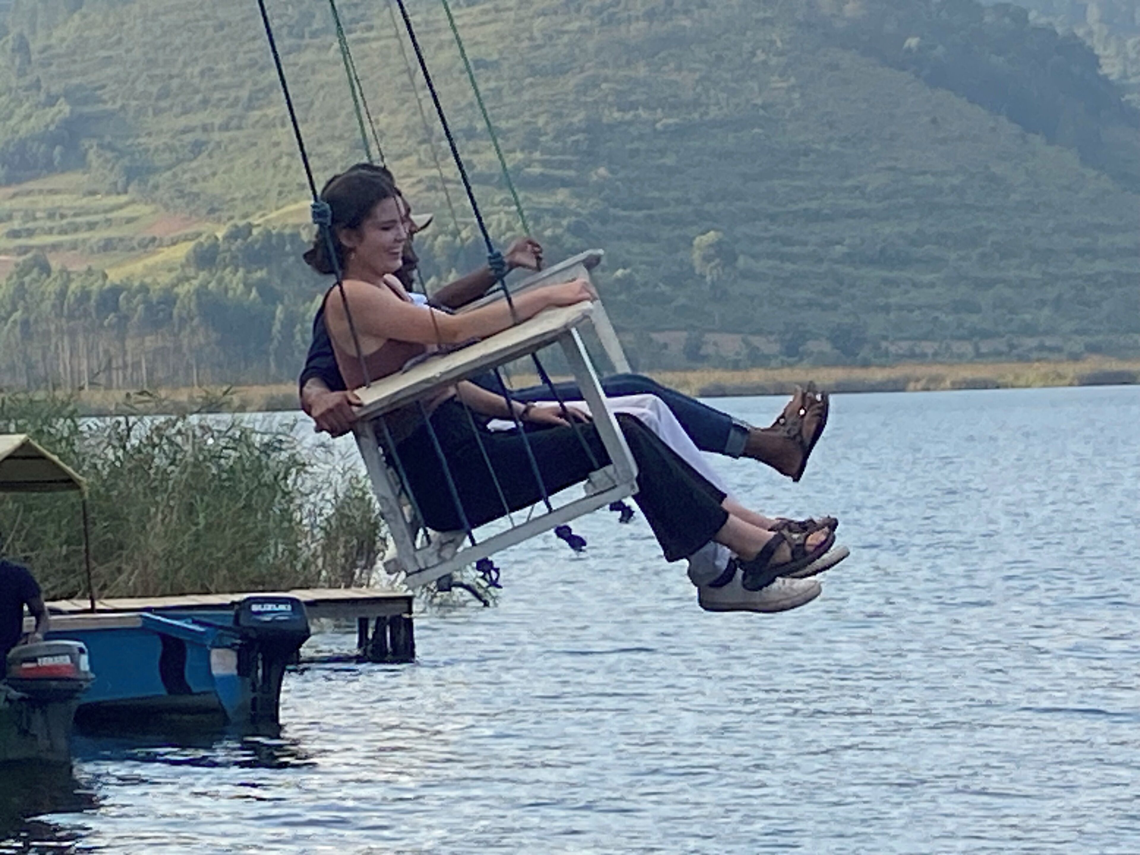 Une personne est assise sur une balançoire au-dessus de l’eau, avec une jetée en arrière-plan.