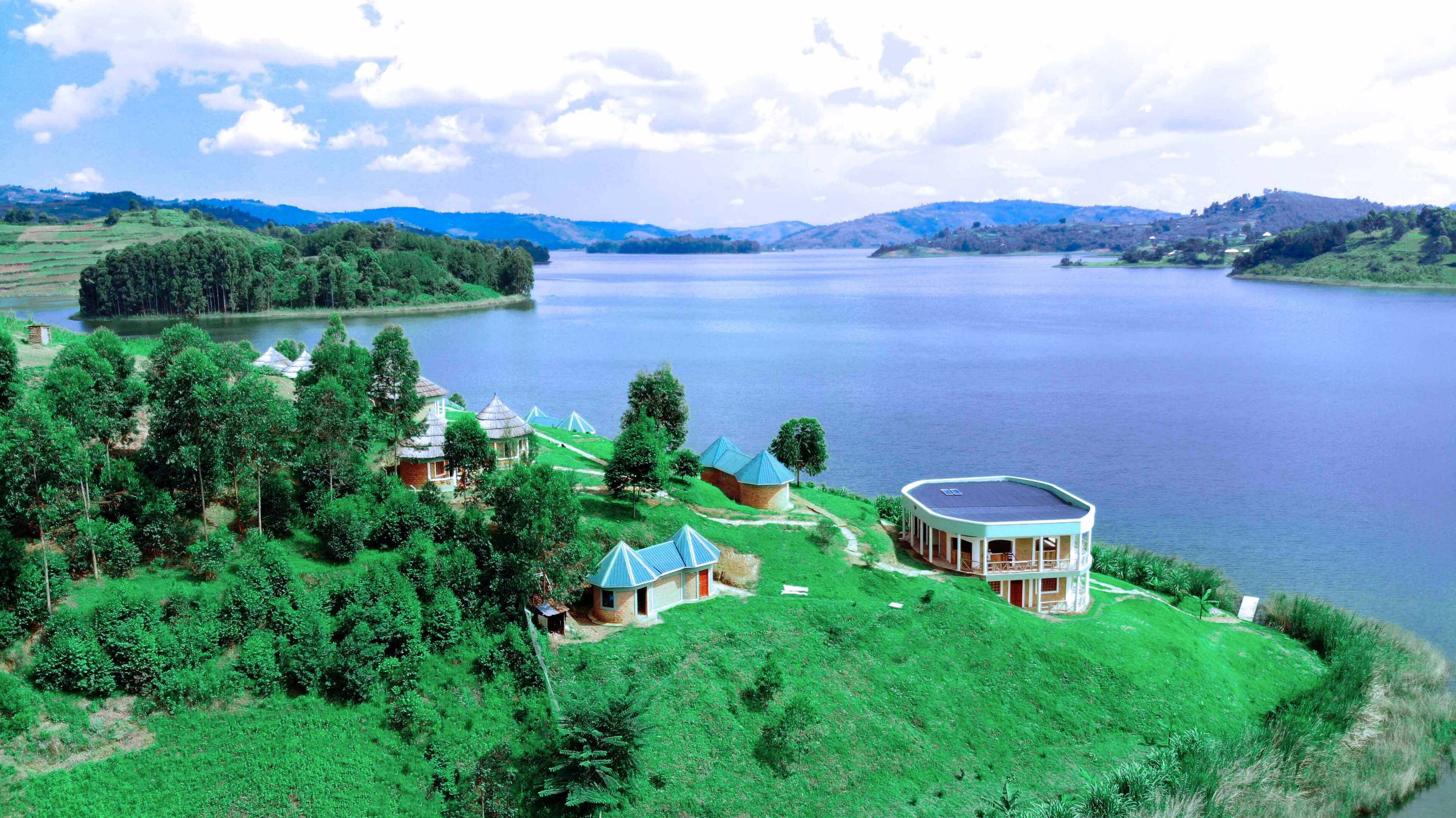 A lakeside property with multiple buildings, including a large house with a curved roof and smaller structures, surrounded by lush greenery and a calm lake.