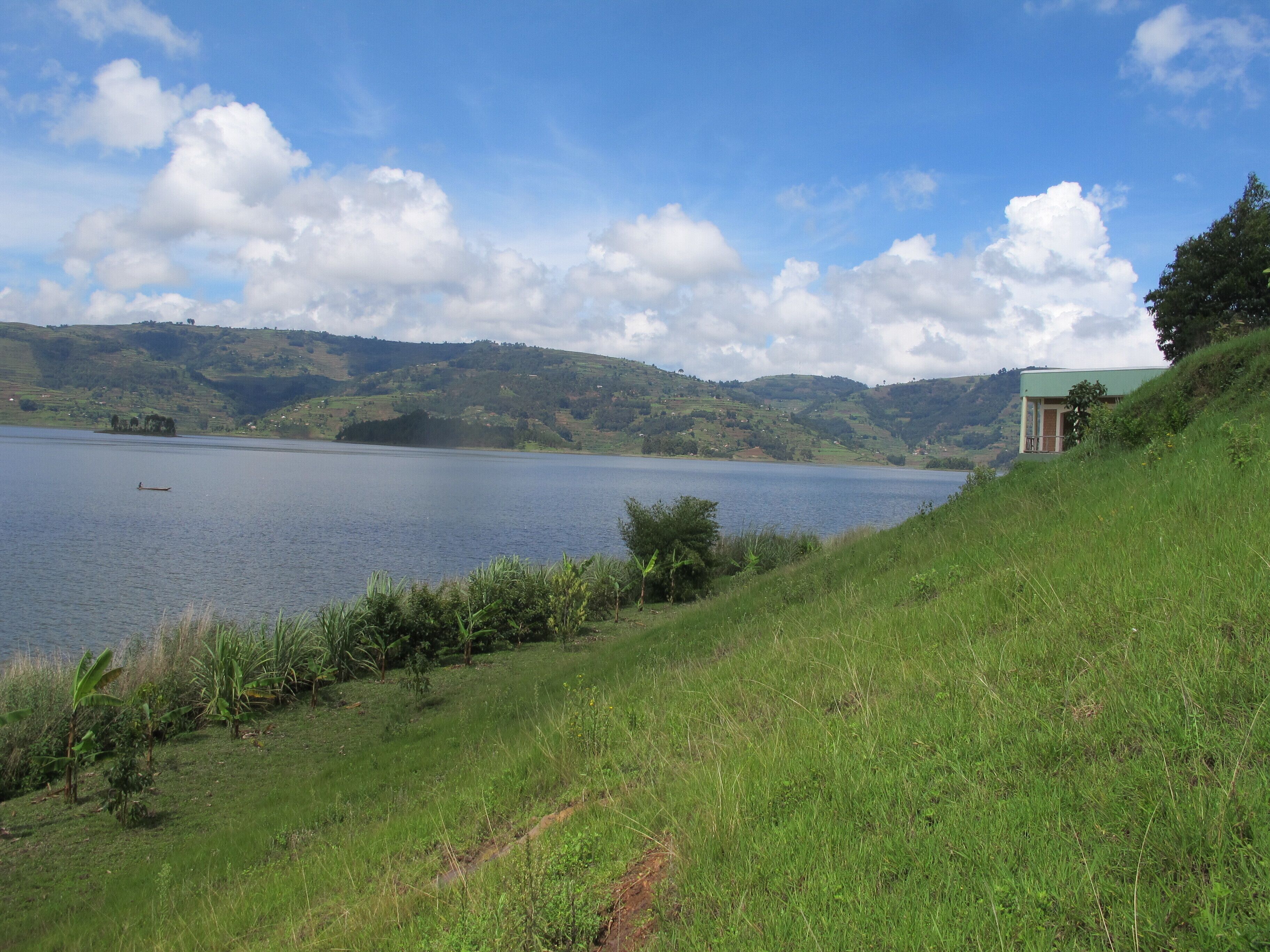 A serene lake with a small boat, surrounded by lush green hills and a clear sky.