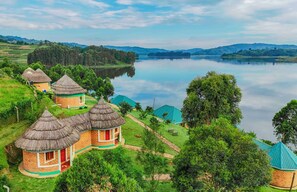 A cluster of traditional thatched-roof houses with a lake in the background. - Nyamunyonyi Lake Resort (Rubanda)