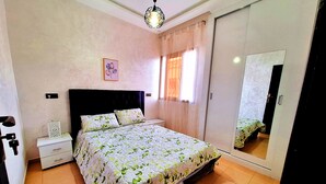 A bedroom with a bed, a nightstand, a wardrobe, a mirror, and a hanging light fixture. - Calm apartment, close to the beach + Chocolat gift
 (Agadir)