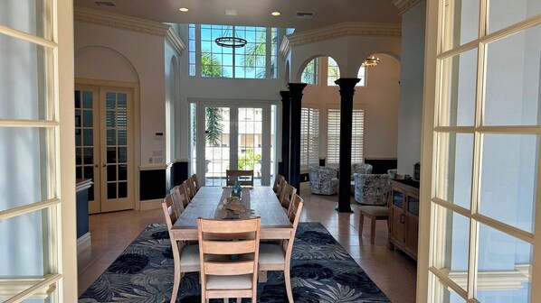 A spacious dining area with a long table and chairs, a patterned rug, and a view through a glass door to an outdoor area.