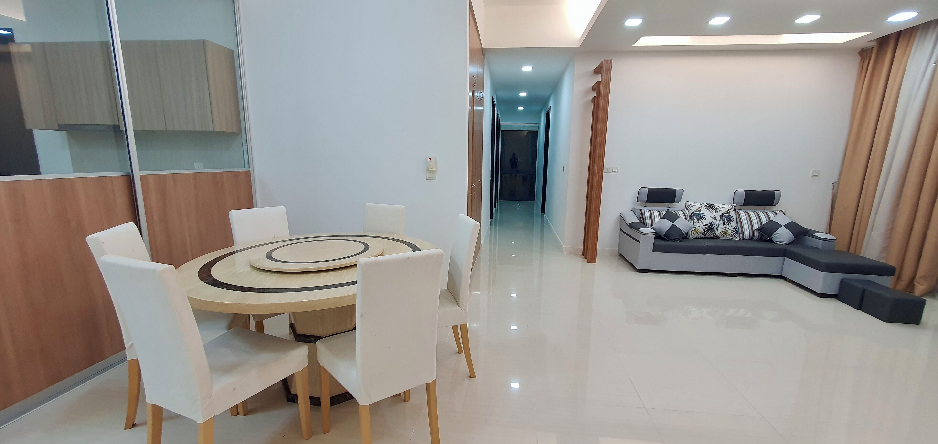 A modern living room with a sofa, a dining table with chairs, and a hallway leading to another room.