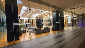 A modern lobby with glass walls, a seating area with sofas and a coffee table, and signs indicating 'Tower A' and 'Tower B'. - The Elements at Jalan Ampang (Kuala Lumpur)