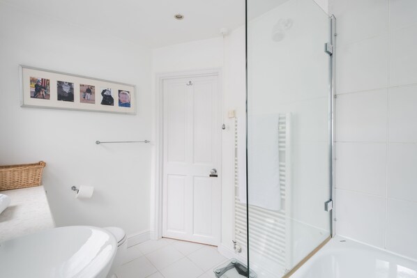 Et moderne badeværelse med toilet i hvidt, glasvæg omkring brusebad og en billedcollage på væggen.