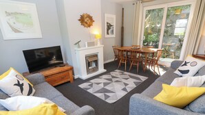 Een woonkamer met grijze banken, een televisie, een open haard en een eethoek met een tafel en stoelen.