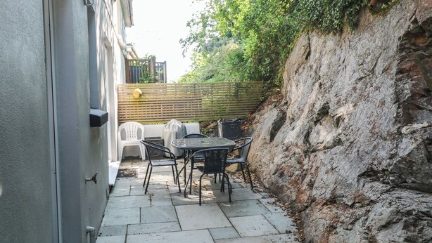 Een terras met een tafel en stoelen, een overdekte barbecue en een stenen muur.