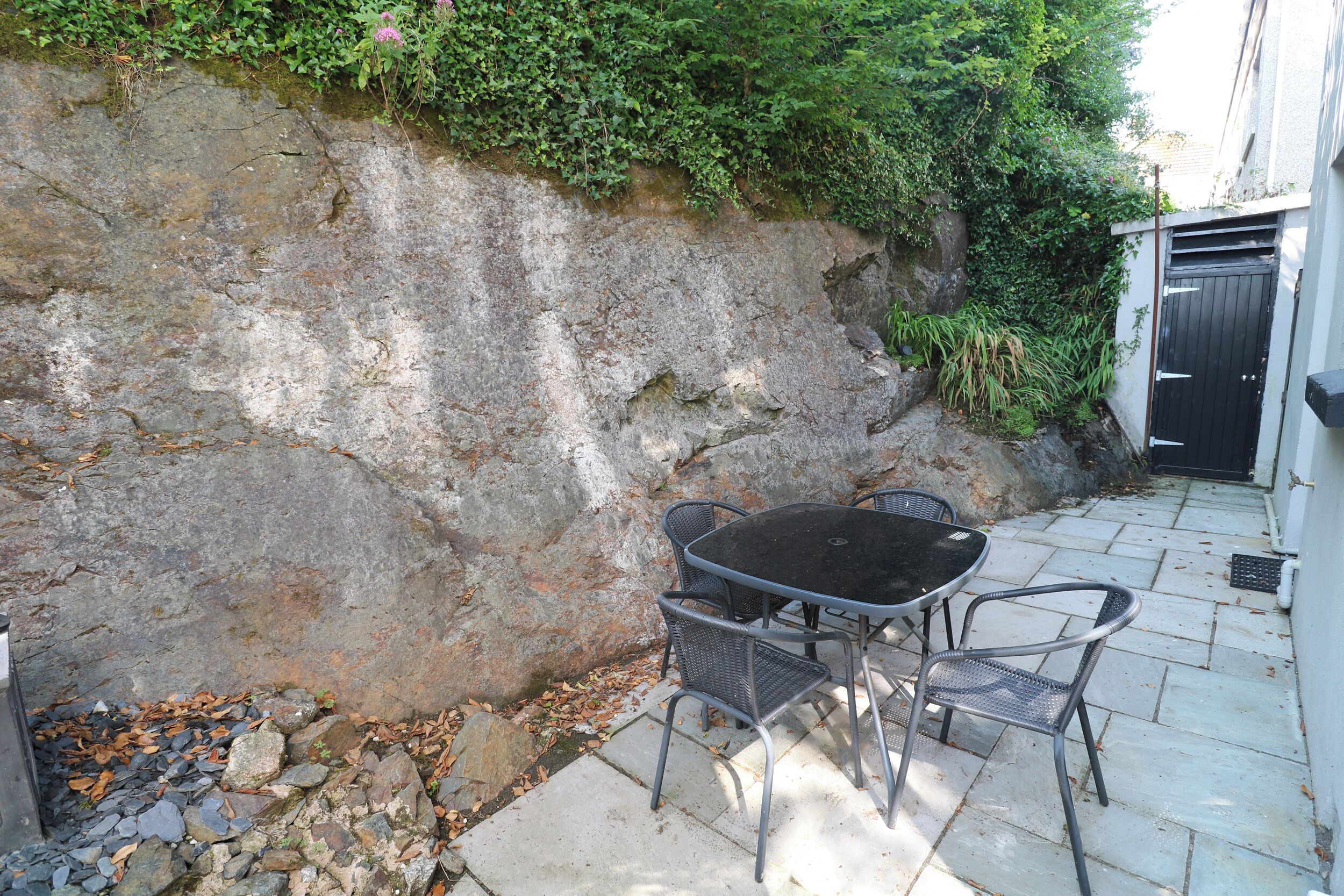 Une terrasse avec une table et des chaises en pierre, un mur en pierre et une porte noire.