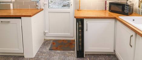A modern kitchen with white cabinets, a wooden countertop, a black microwave, and a sink.