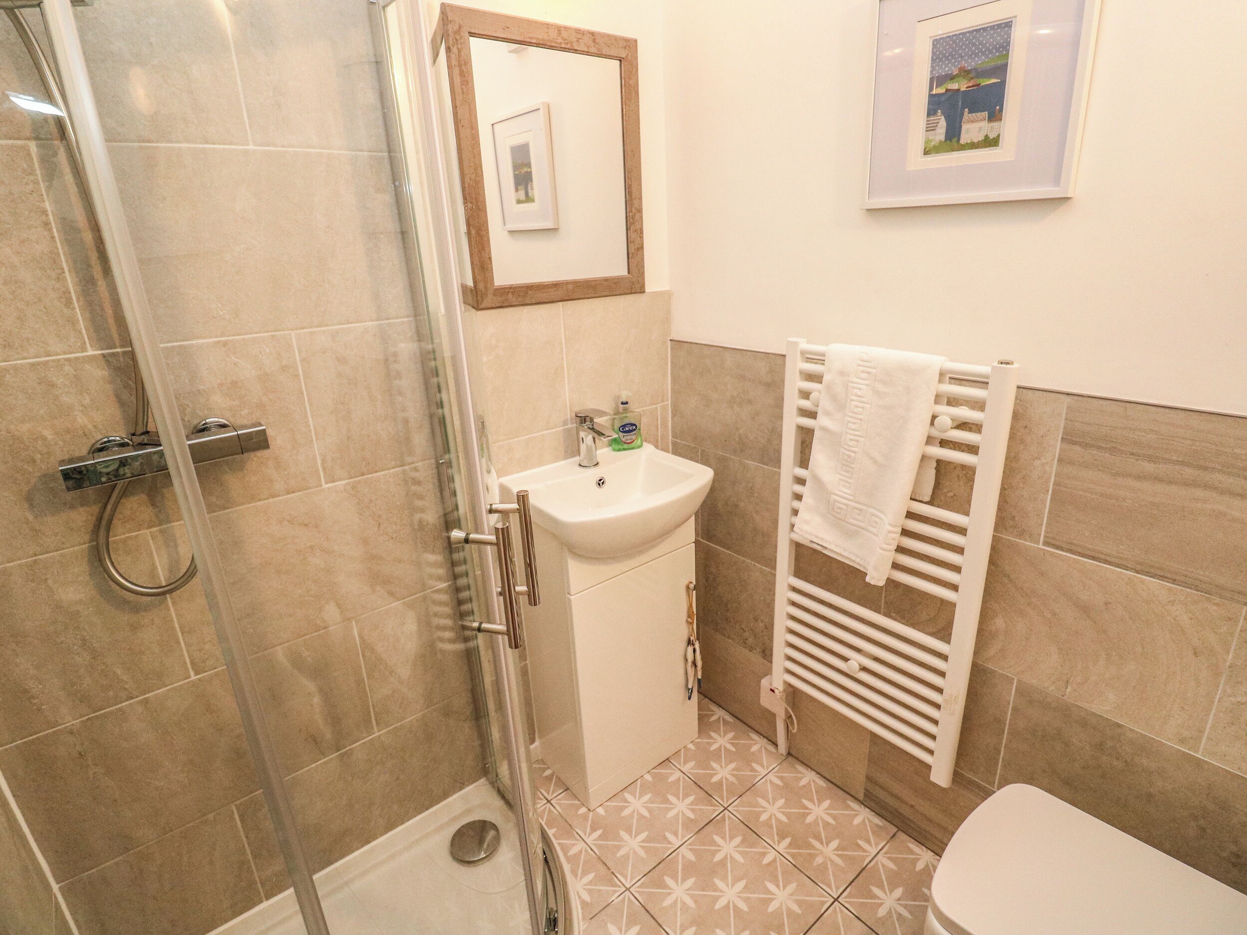 A bathroom with a glass shower enclosure, a white sink, and a towel rack.