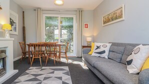 Een woonkamer met een grijze bank, een geometrisch vloerkleed, houten stoelen, een tafel en uitzicht door een glazen deur.