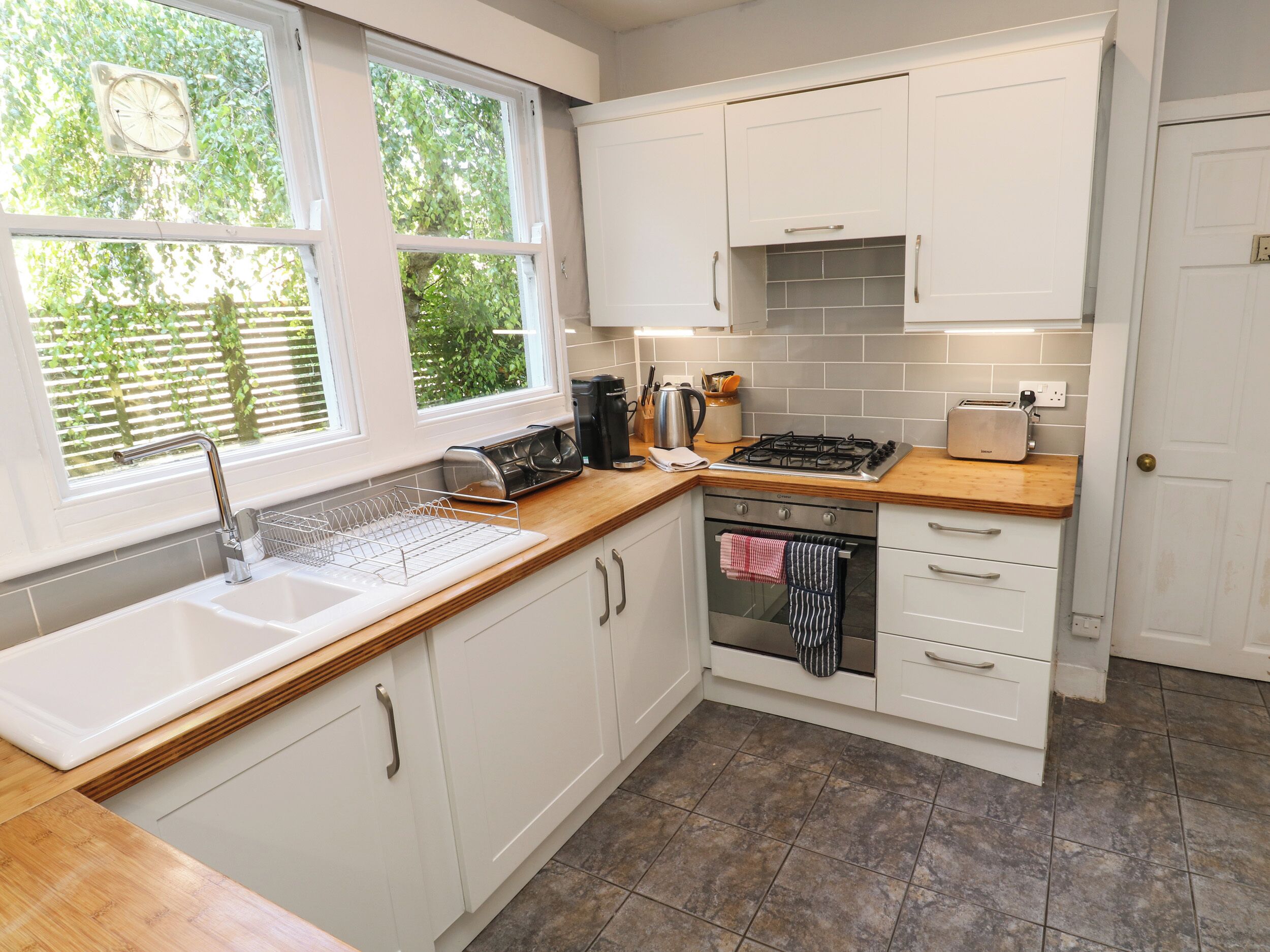 A modern kitchen with white cabinets, a wooden countertop, a gas stove, a sink, and a window with a view of greenery.