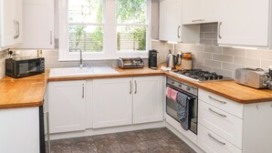Een moderne keuken met witte kastjes, een houten aanrecht, een fornuis, een magnetron en een spoelbak.