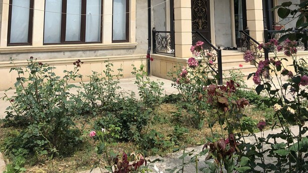 Ein zweistöckiges Haus mit Balkon, großen Fenstern und einem Blumenbeet.