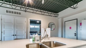 A modern kitchen with a stainless steel sink, white cabinets, and a large window. - The Cartier Lux DT Apt w/Skyline View (Des Moines)