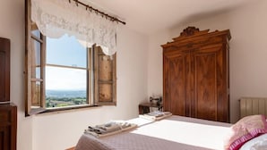 Une chambre avec une grande fenêtre, une armoire en bois et un lit avec un oreiller rose.