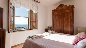 Une chambre avec une grande fenêtre, une armoire en bois et un lit avec un oreiller rose.