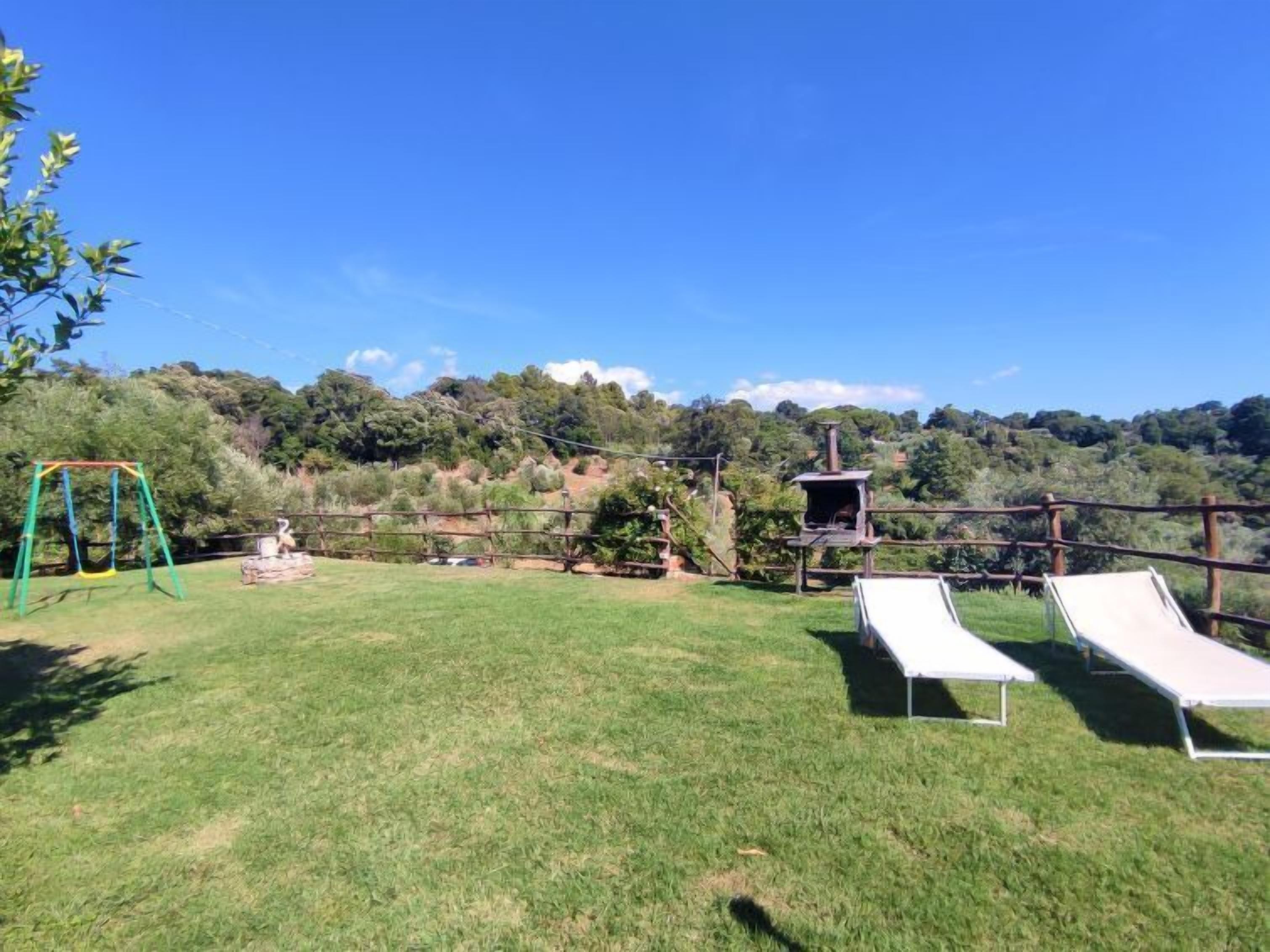 A grassy backyard with a swing set, a small playhouse, and two lounge chairs.