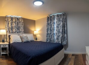 A neatly arranged bedroom with a bed, two bedside tables with lamps, and patterned curtains. - 3BedroomApt Pool CampFire PlayArea (Bar Harbor)