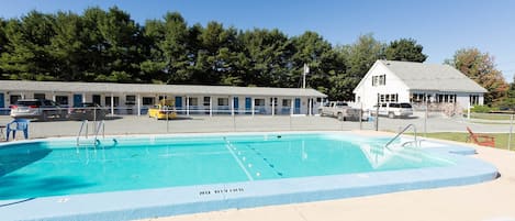 Una piscina con un cartel de 'No Diving', sillas de descanso y un motel al fondo.