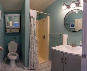 A bathroom with a toilet, shower, sink, and a cabinet with wicker baskets. - 3BedroomApt Pool CampFire PlayArea (Bar Harbor)