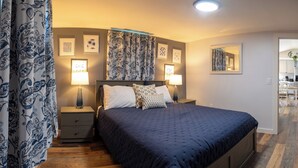 A bedroom with a large bed, two bedside tables with lamps, patterned curtains, and framed artwork on the walls. - 3BedroomApt Pool CampFire PlayArea (Bar Harbor)
